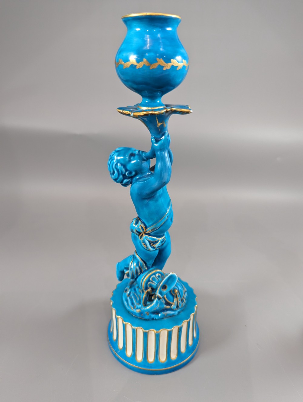 A pair of turquoise blue glazed porcelain candlesticks shaped as cherubs supporting urn sockets on fluted bases with gold trim. View V
