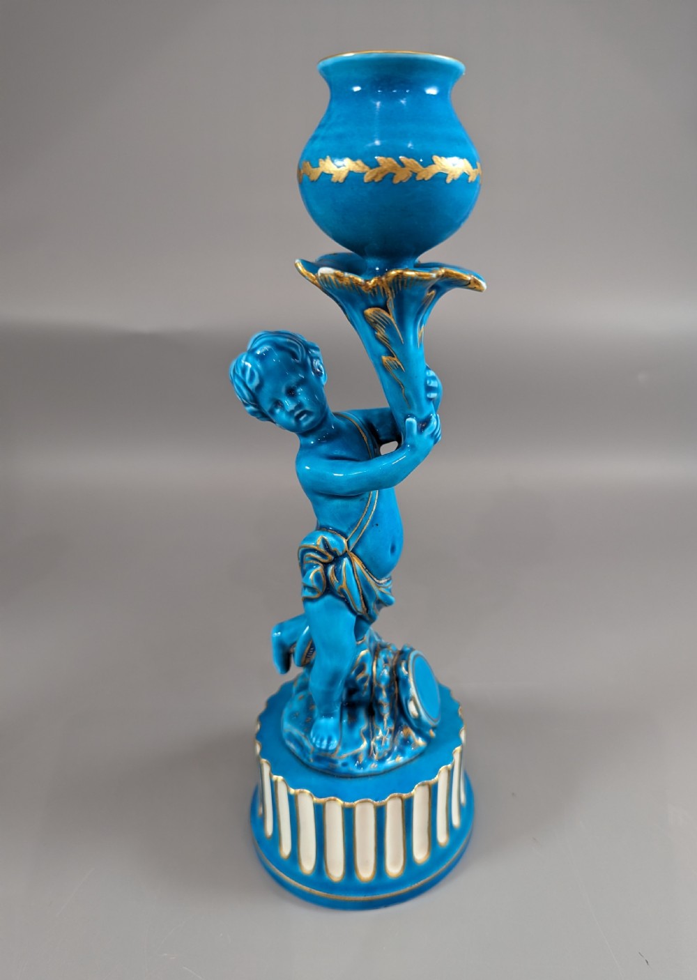 A pair of turquoise blue glazed porcelain candlesticks shaped as cherubs supporting urn sockets on fluted bases with gold trim. View VIII