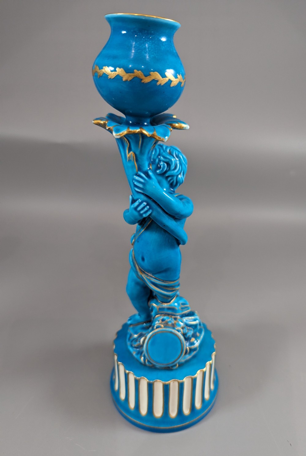 A pair of turquoise blue glazed porcelain candlesticks shaped as cherubs supporting urn sockets on fluted bases with gold trim. View IX