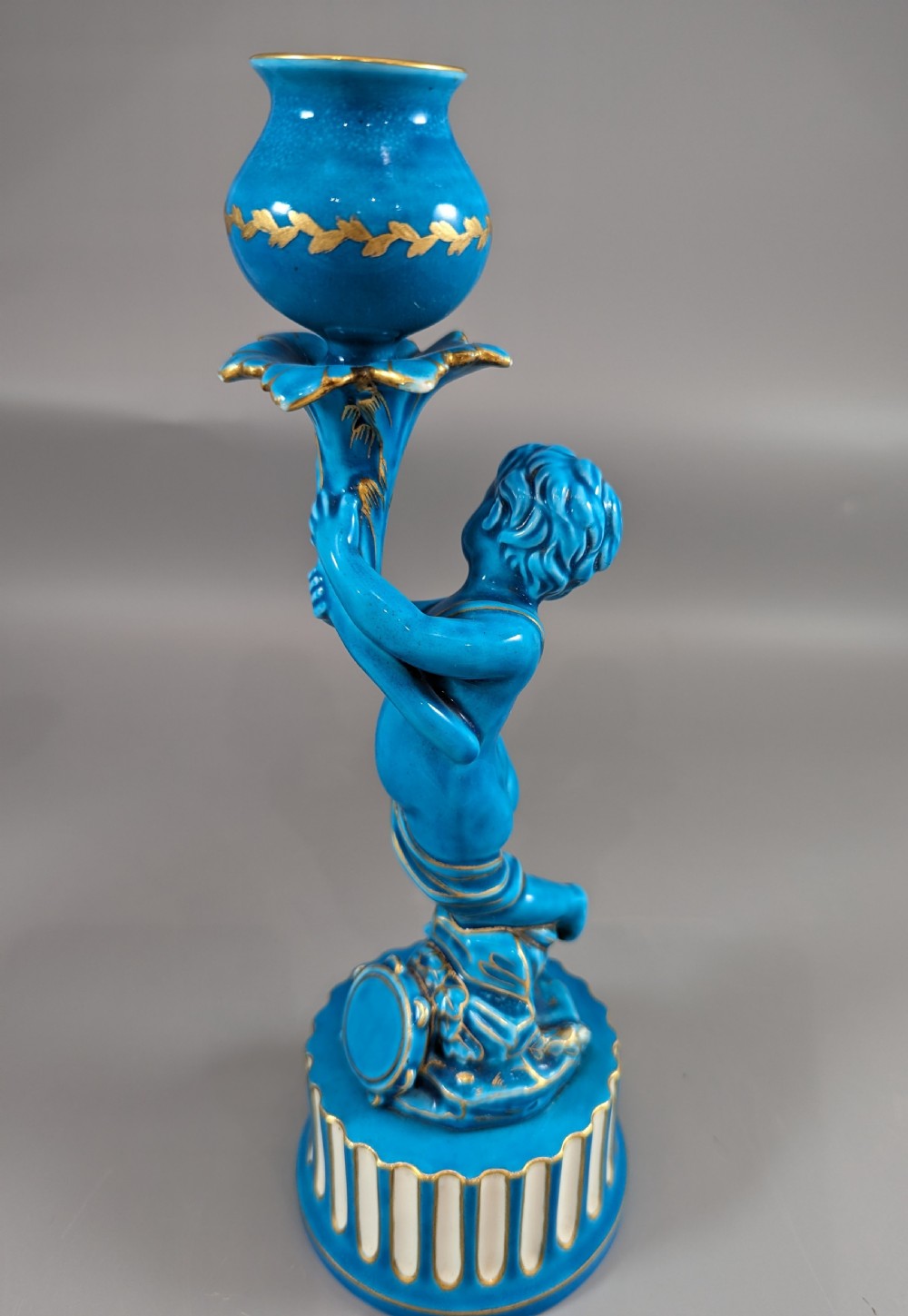 A pair of turquoise blue glazed porcelain candlesticks shaped as cherubs supporting urn sockets on fluted bases with gold trim. View X