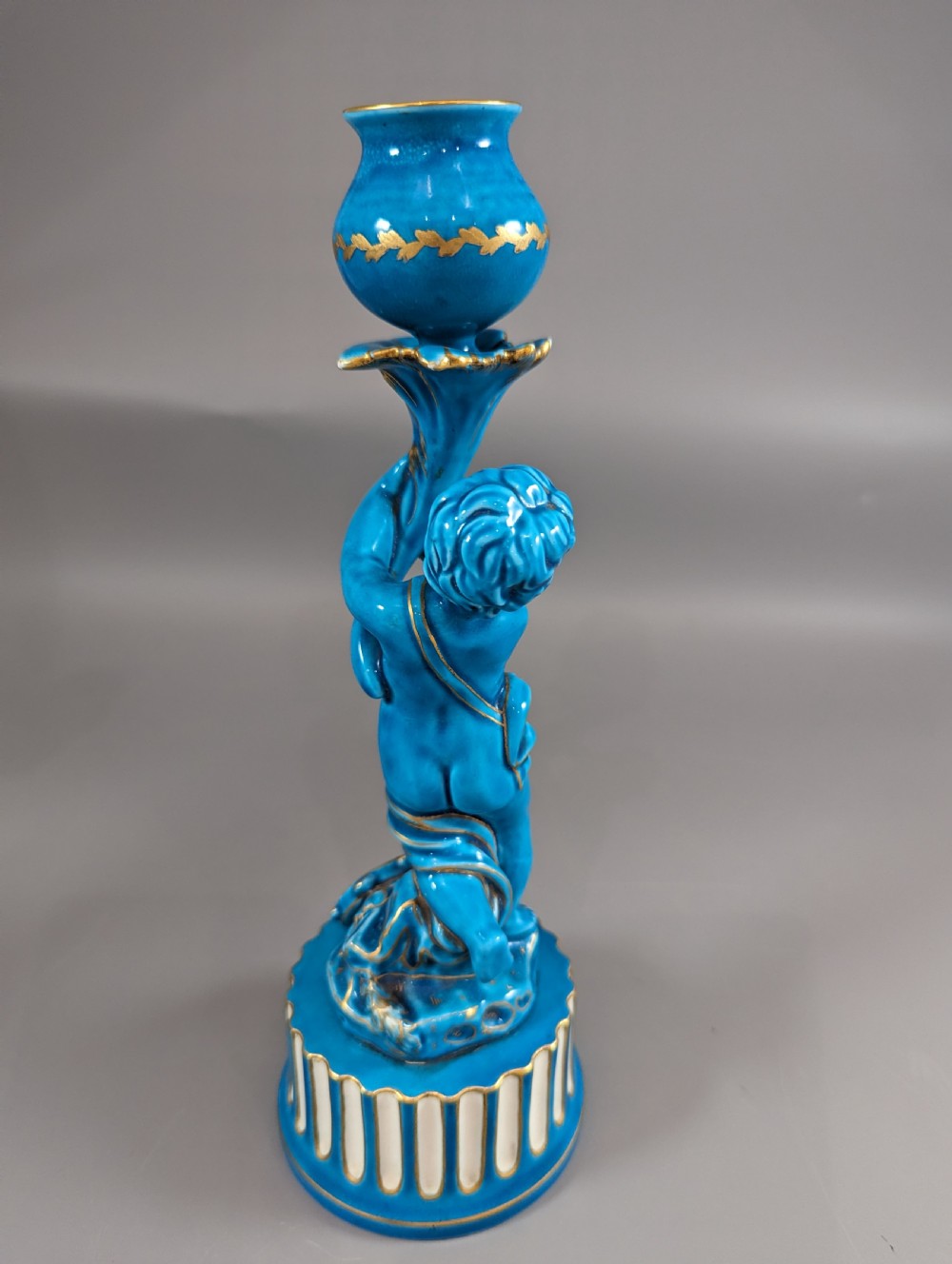 A pair of turquoise blue glazed porcelain candlesticks shaped as cherubs supporting urn sockets on fluted bases with gold trim. View XI