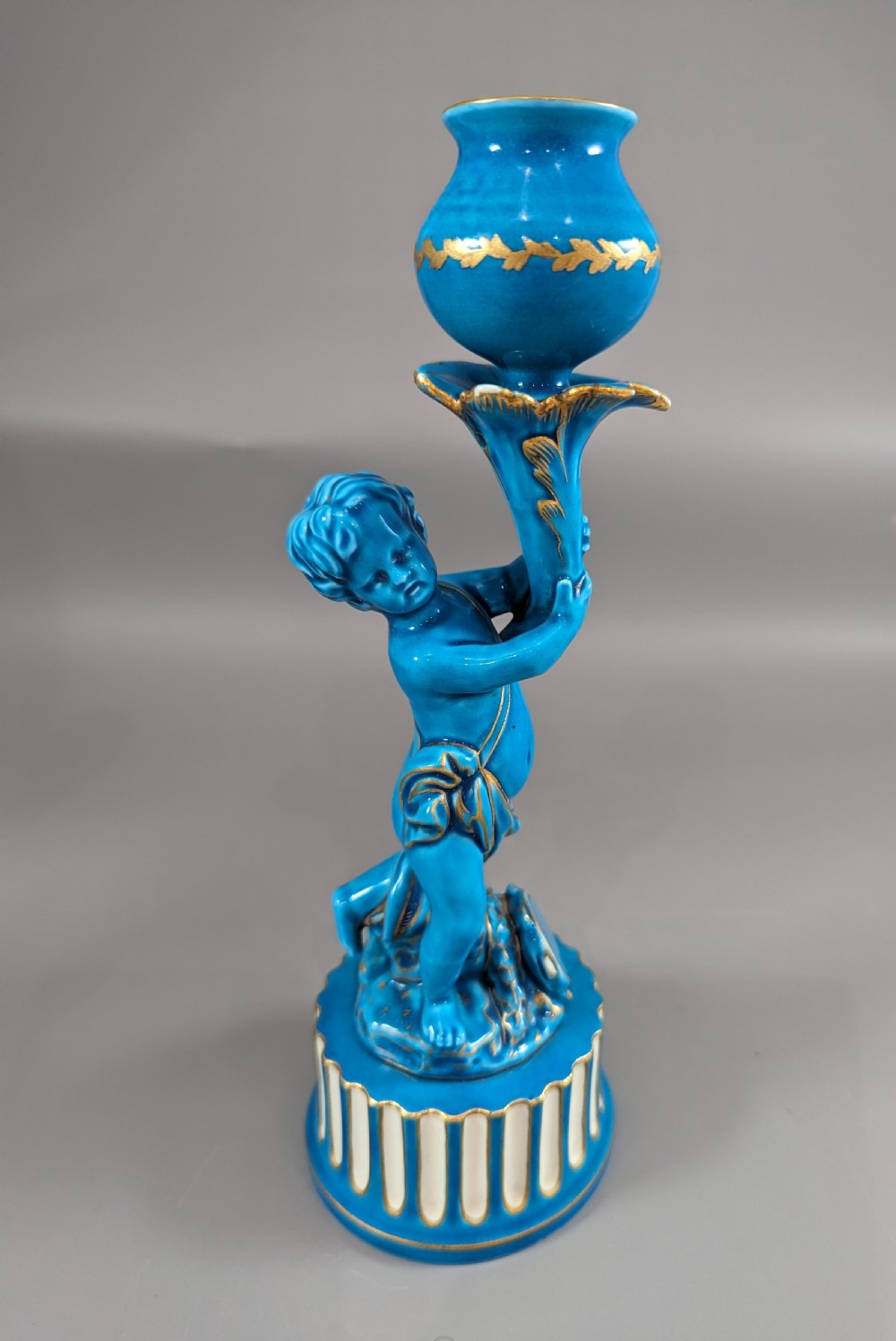 A pair of turquoise blue glazed porcelain candlesticks shaped as cherubs supporting urn sockets on fluted bases with gold trim. View XII