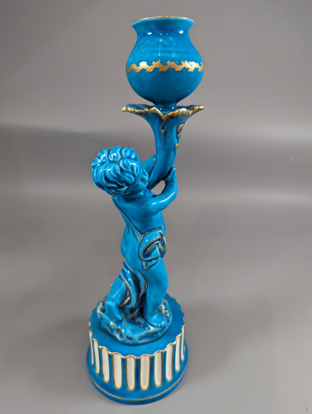 A pair of turquoise blue glazed porcelain candlesticks shaped as cherubs supporting urn sockets on fluted bases with gold trim. View XIV