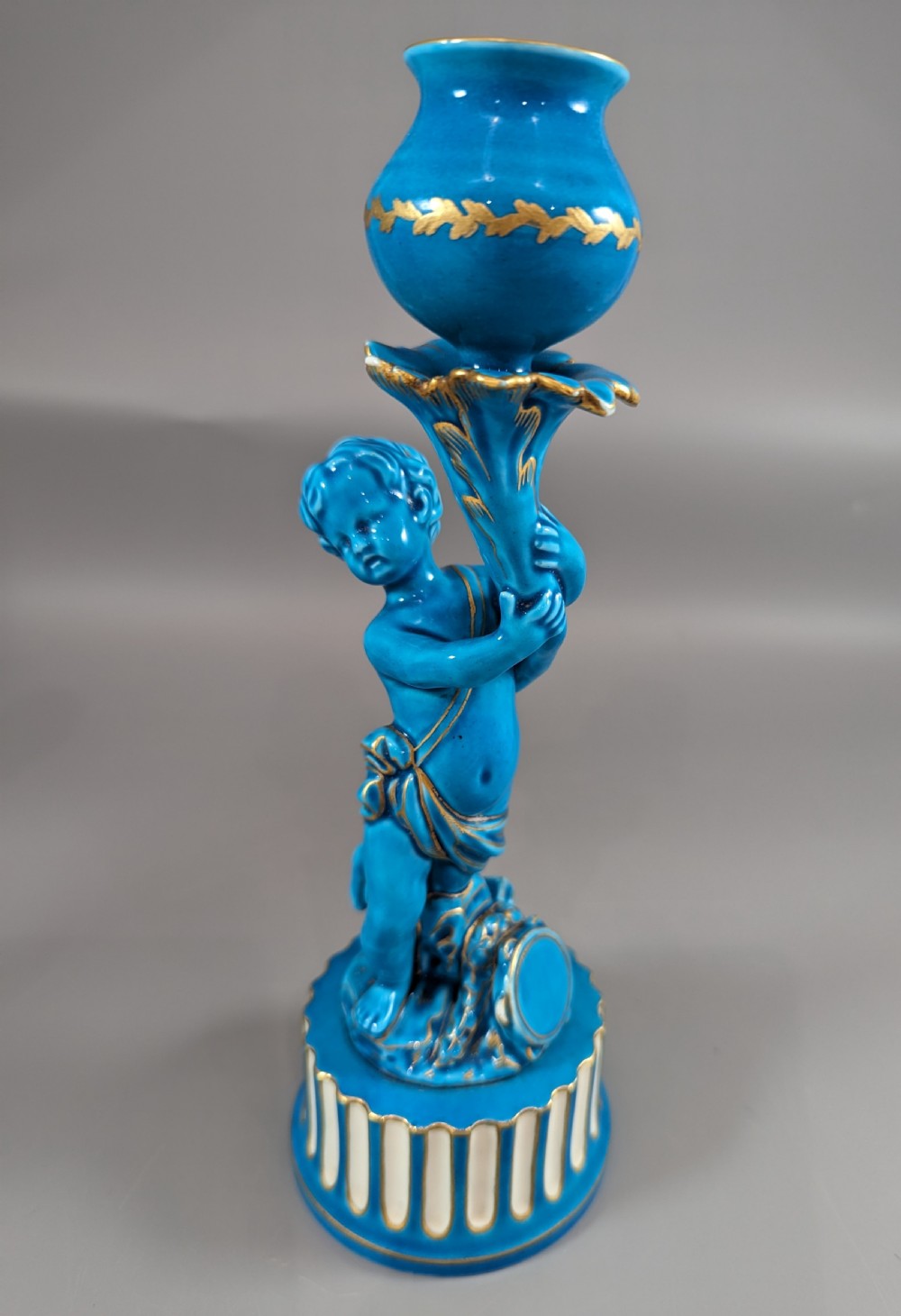 A pair of turquoise blue glazed porcelain candlesticks shaped as cherubs supporting urn sockets on fluted bases with gold trim. View XV