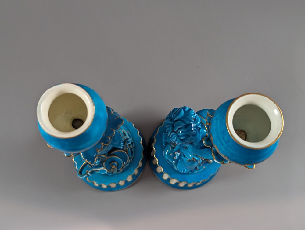 A pair of turquoise blue glazed porcelain candlesticks shaped as cherubs supporting urn sockets on fluted bases with gold trim. View XVII