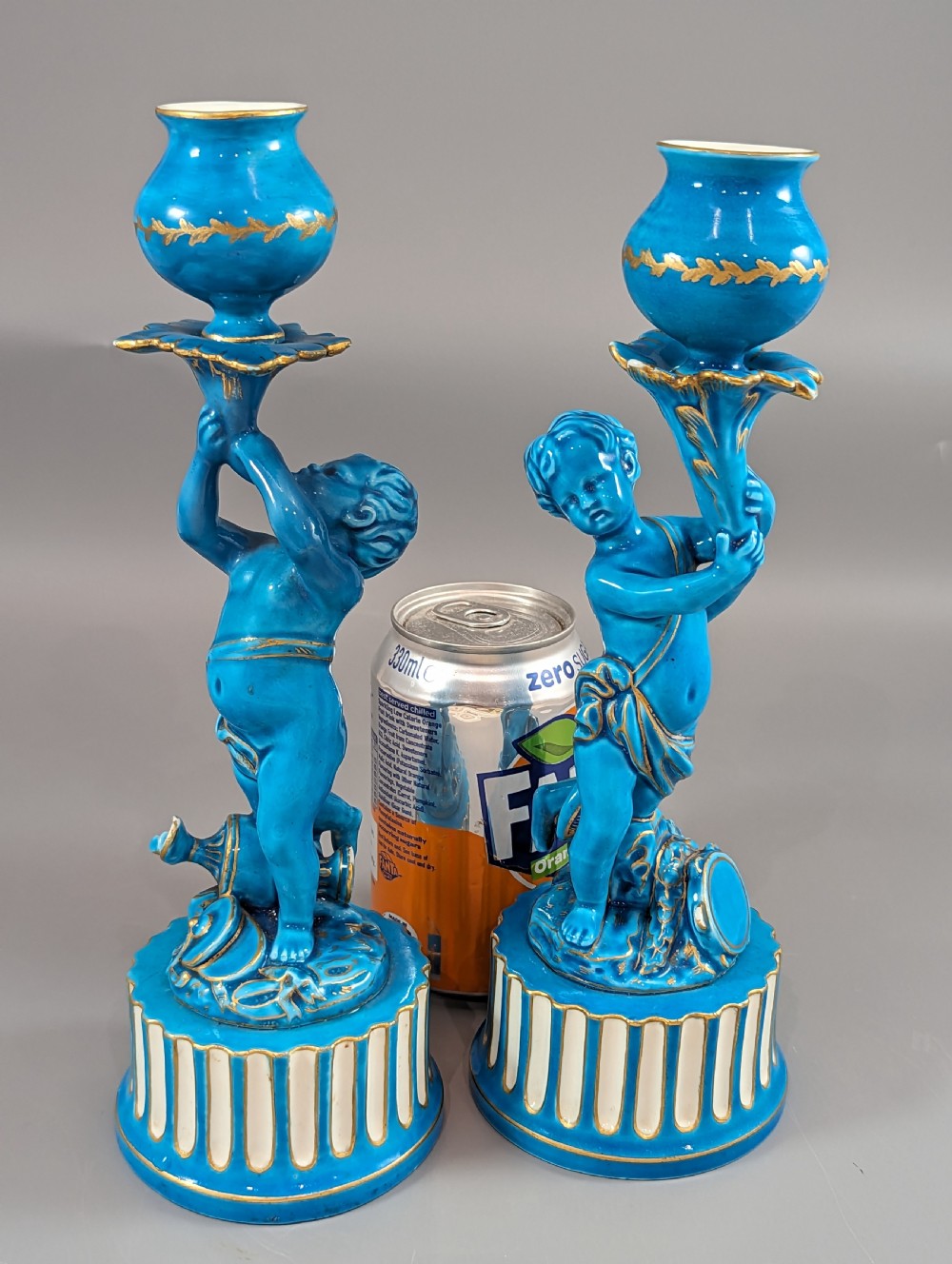 A pair of turquoise blue glazed porcelain candlesticks shaped as cherubs supporting urn sockets on fluted bases with gold trim. View XXIII