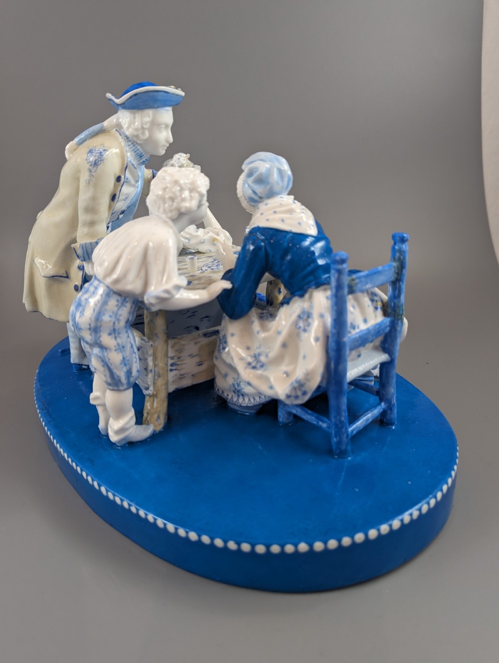 Late 19th-century French blue and white glazed porcelain figurine group depicting four figures gathered around a table fortune-telling on an oval blue base. View VI