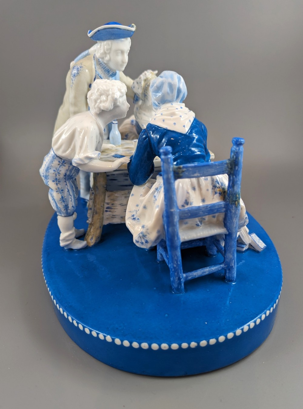 Late 19th-century French blue and white glazed porcelain figurine group depicting four figures gathered around a table fortune-telling on an oval blue base. View VII
