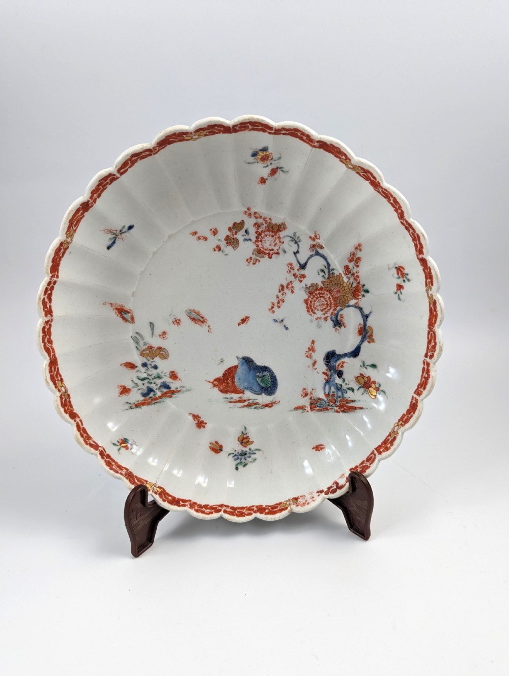 A circular fluted soft-paste porcelain dish decorated with the Kakiemon quail pattern in iron-red, blue, and gold enamels on a white ground.