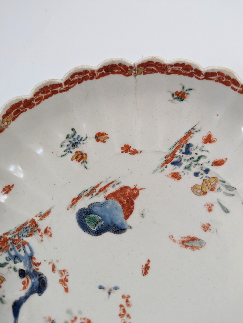 A circular fluted soft-paste porcelain dish decorated with the Kakiemon quail pattern in iron-red, blue, and gold enamels on a white ground. View VI