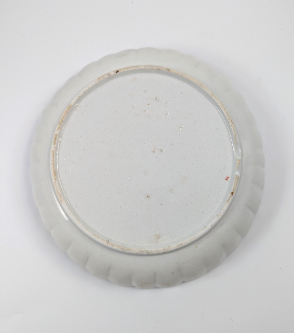 A circular fluted soft-paste porcelain dish decorated with the Kakiemon quail pattern in iron-red, blue, and gold enamels on a white ground. View VII