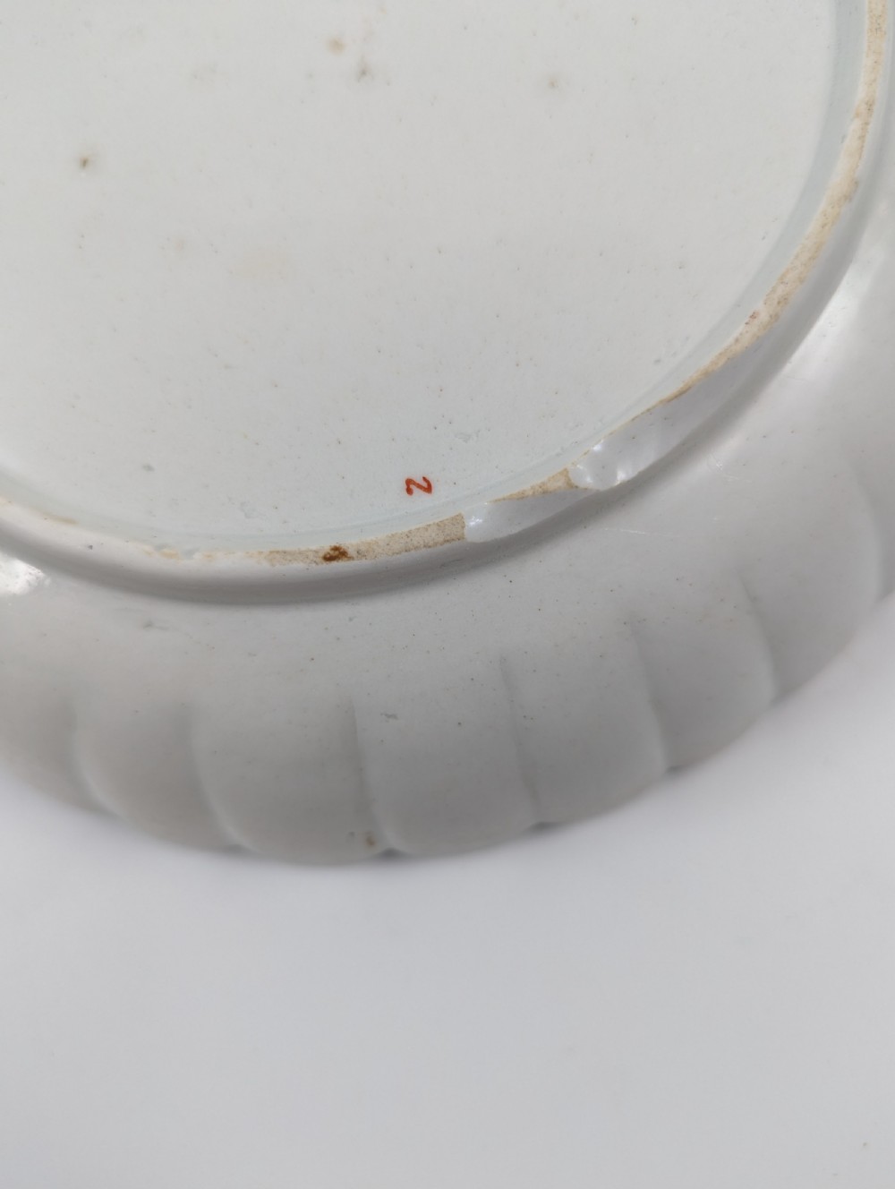 A circular fluted soft-paste porcelain dish decorated with the Kakiemon quail pattern in iron-red, blue, and gold enamels on a white ground. View VIII