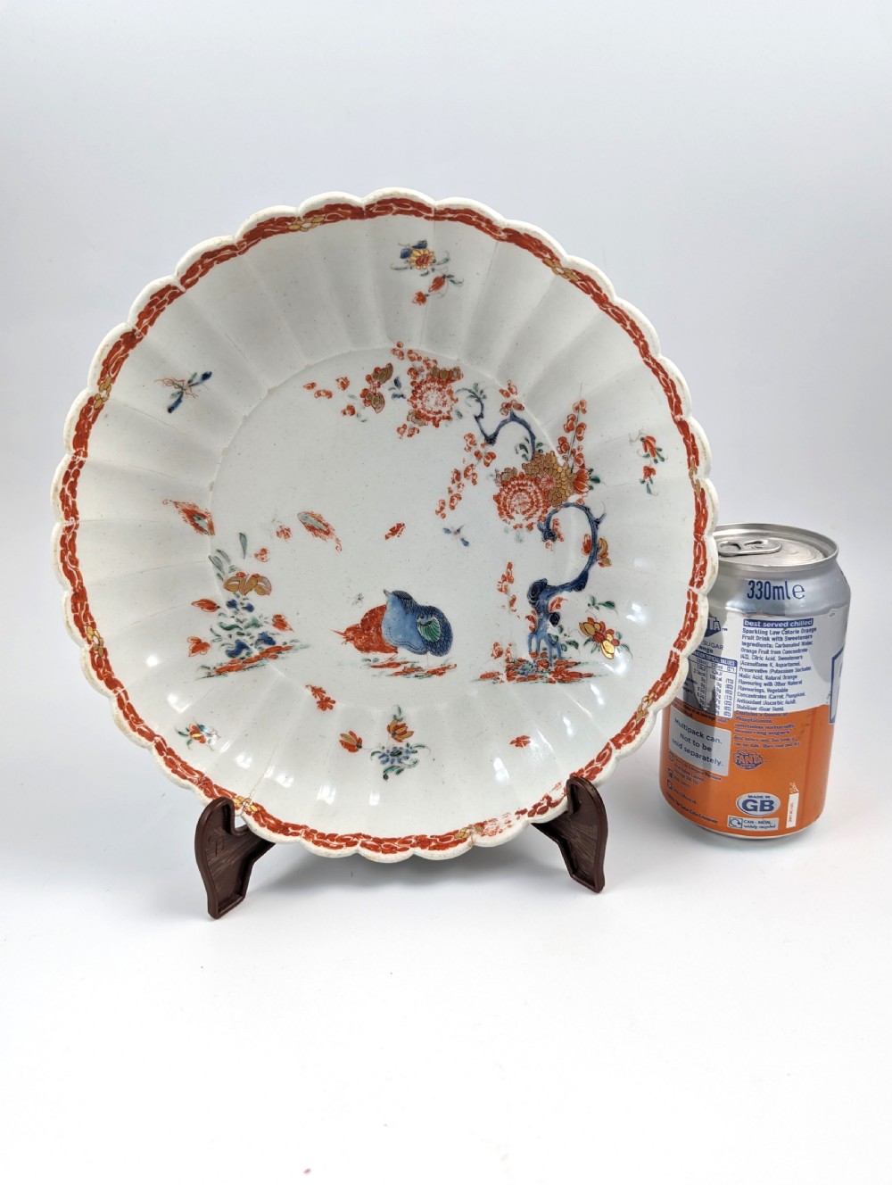 A circular fluted soft-paste porcelain dish decorated with the Kakiemon quail pattern in iron-red, blue, and gold enamels on a white ground. View IX