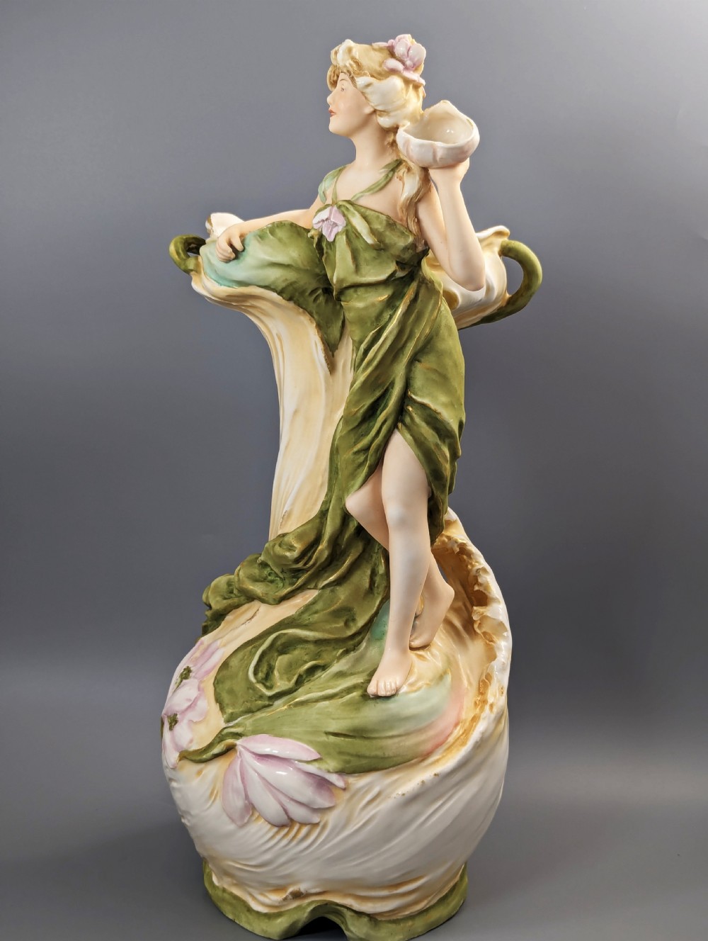 An Art Nouveau Royal Dux porcelain vase depicting a draped water nymph holding a seashell against flowing foliage in cream, olive green, and soft pink shades. View II