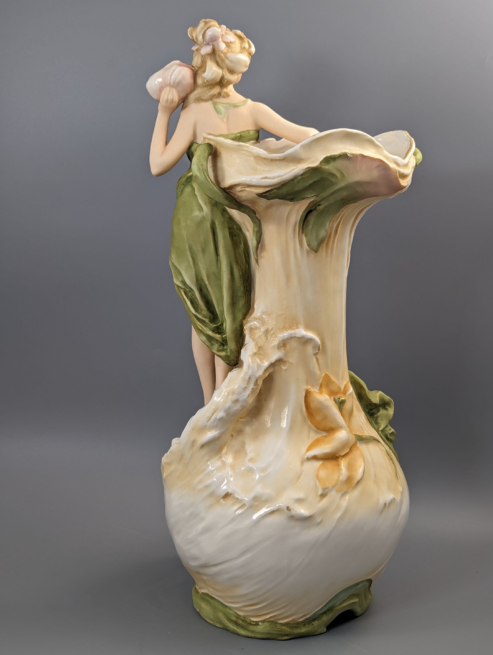 An Art Nouveau Royal Dux porcelain vase depicting a draped water nymph holding a seashell against flowing foliage in cream, olive green, and soft pink shades. View IV