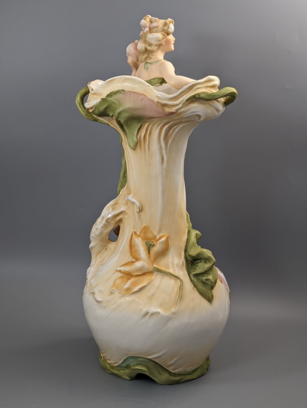An Art Nouveau Royal Dux porcelain vase depicting a draped water nymph holding a seashell against flowing foliage in cream, olive green, and soft pink shades. View V