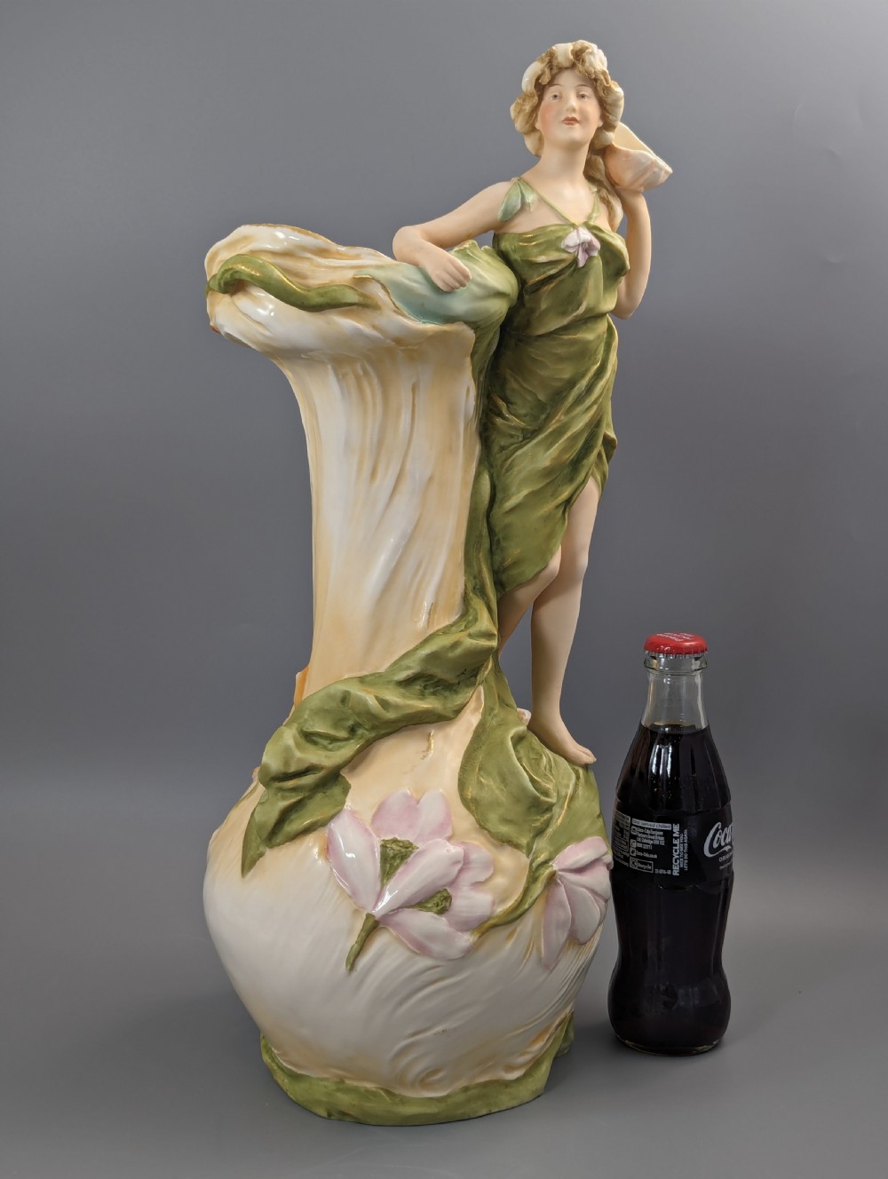 An Art Nouveau Royal Dux porcelain vase depicting a draped water nymph holding a seashell against flowing foliage in cream, olive green, and soft pink shades. View X
