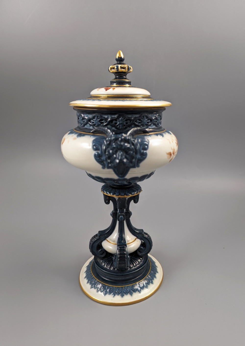 A late Victorian cream and dark blue porcelain pedestal urn decorated with hand-painted sepia floral panels, dark scroll handles, a matching lid, and gilded accents. View III