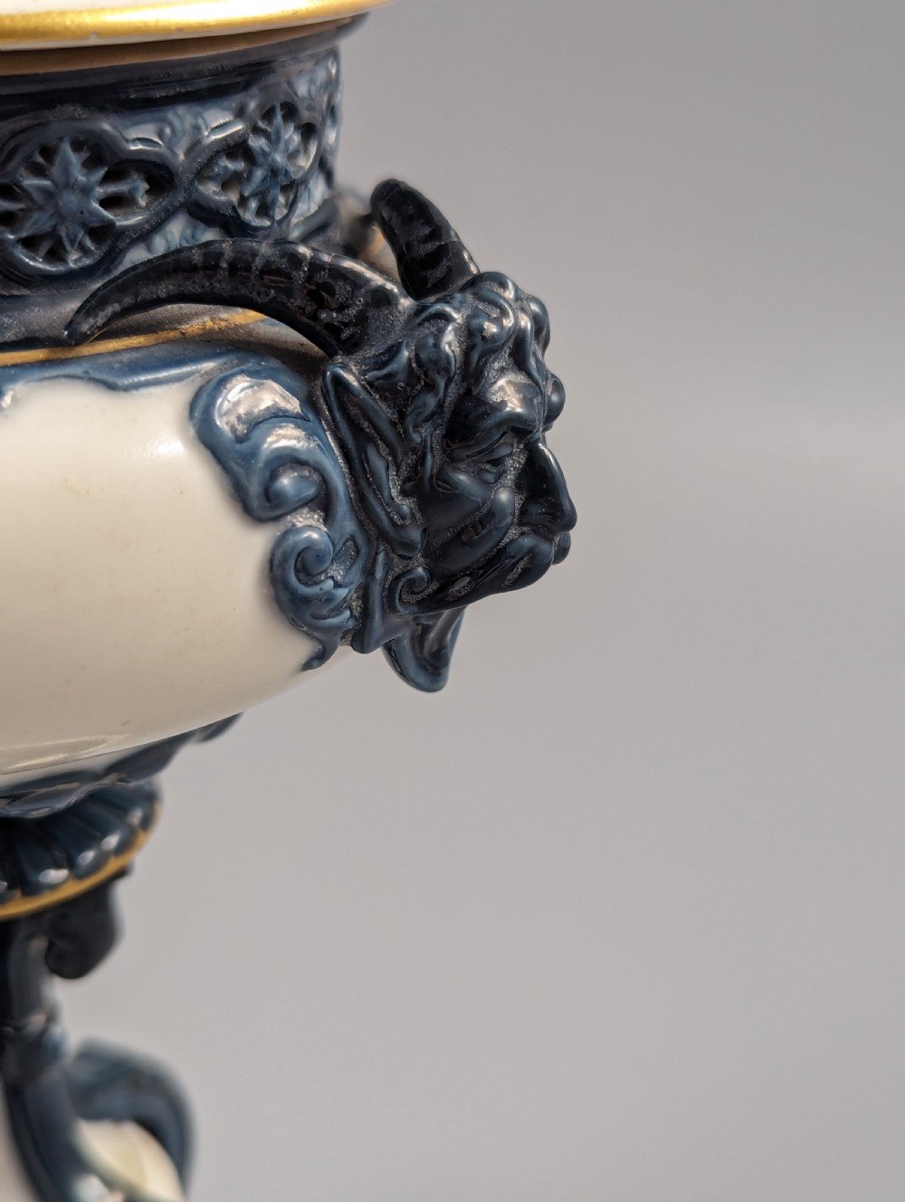 A late Victorian cream and dark blue porcelain pedestal urn decorated with hand-painted sepia floral panels, dark scroll handles, a matching lid, and gilded accents. View IX