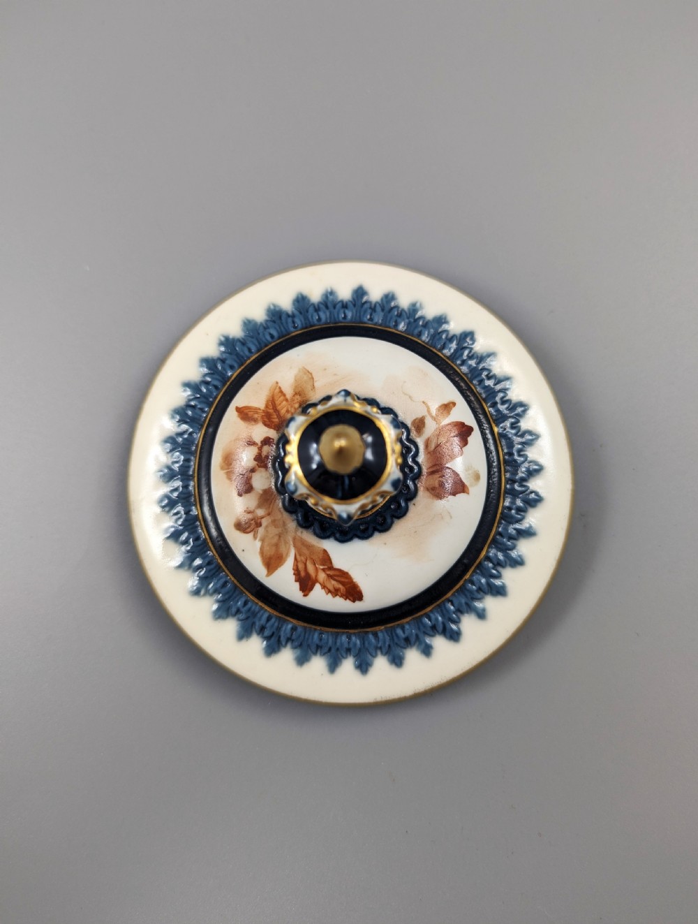 A late Victorian cream and dark blue porcelain pedestal urn decorated with hand-painted sepia floral panels, dark scroll handles, a matching lid, and gilded accents. View XII