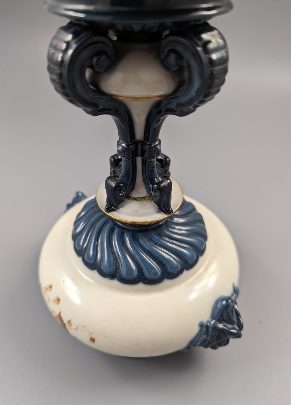 A late Victorian cream and dark blue porcelain pedestal urn decorated with hand-painted sepia floral panels, dark scroll handles, a matching lid, and gilded accents. View XIV