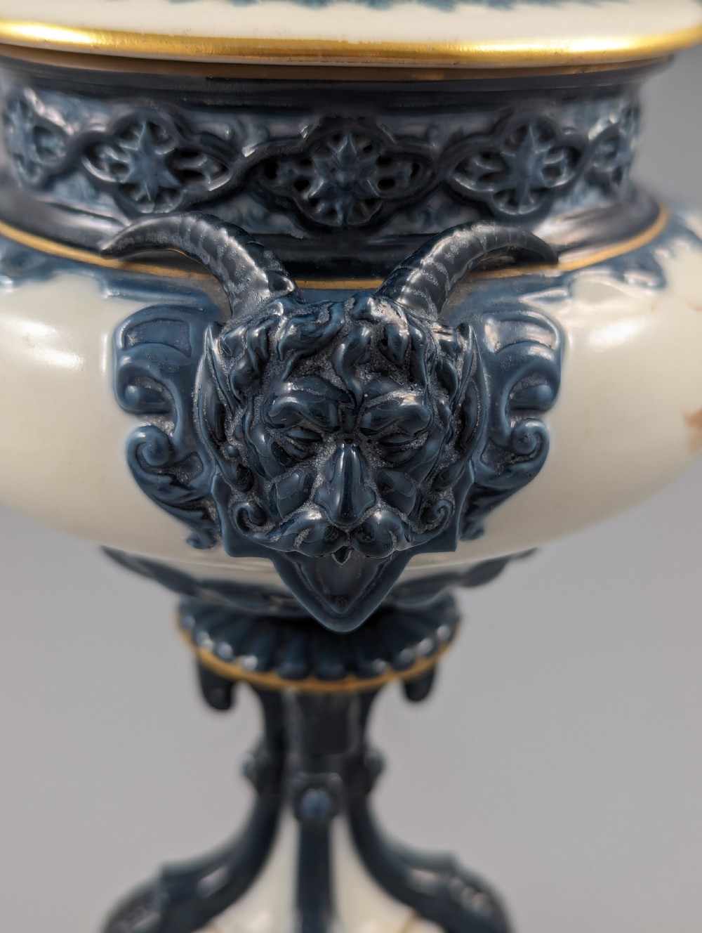 A late Victorian cream and dark blue porcelain pedestal urn decorated with hand-painted sepia floral panels, dark scroll handles, a matching lid, and gilded accents. View XVI