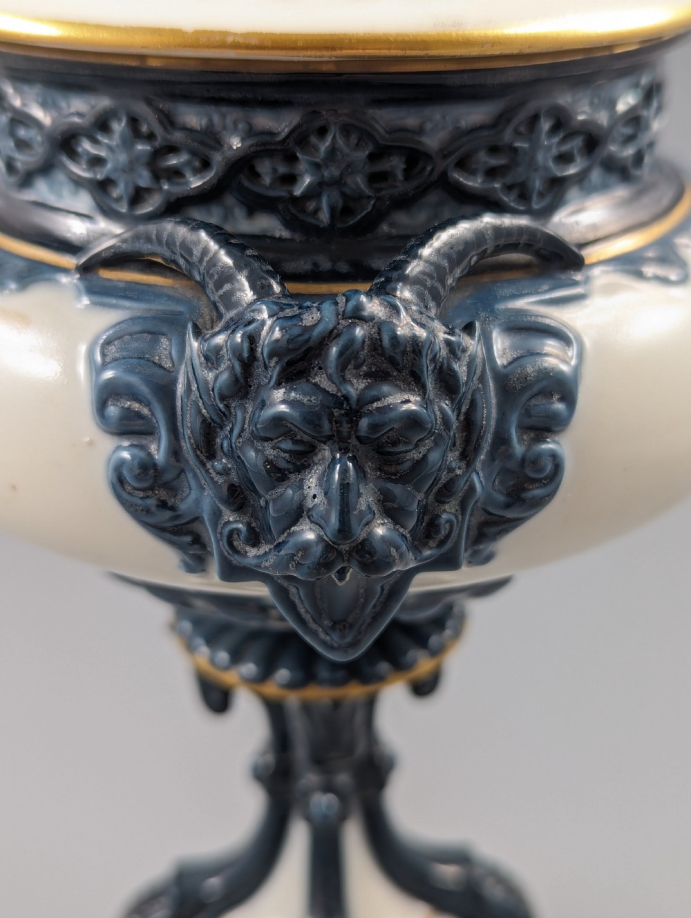 A late Victorian cream and dark blue porcelain pedestal urn decorated with hand-painted sepia floral panels, dark scroll handles, a matching lid, and gilded accents. View XVII
