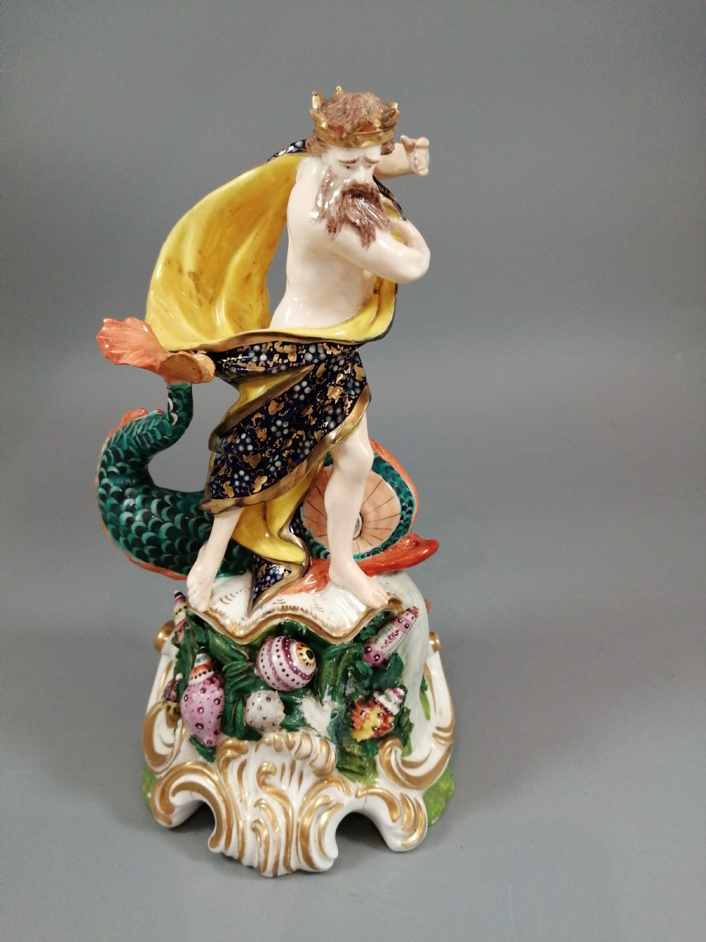 A Bloor Derby porcelain figure of Neptune standing atop a shell and rockwork base with sea creatures, wearing a crown and drapery decorated in gold leaf and blue enamel.