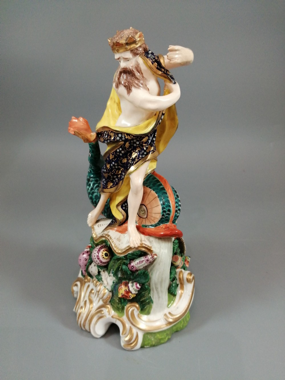 A Bloor Derby porcelain figure of Neptune standing atop a shell and rockwork base with sea creatures, wearing a crown and drapery decorated in gold leaf and blue enamel. View II