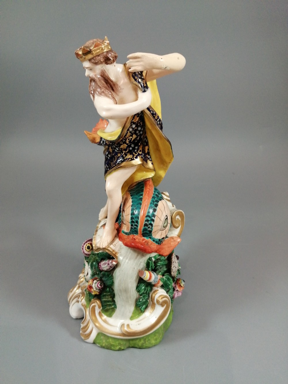 A Bloor Derby porcelain figure of Neptune standing atop a shell and rockwork base with sea creatures, wearing a crown and drapery decorated in gold leaf and blue enamel. View III