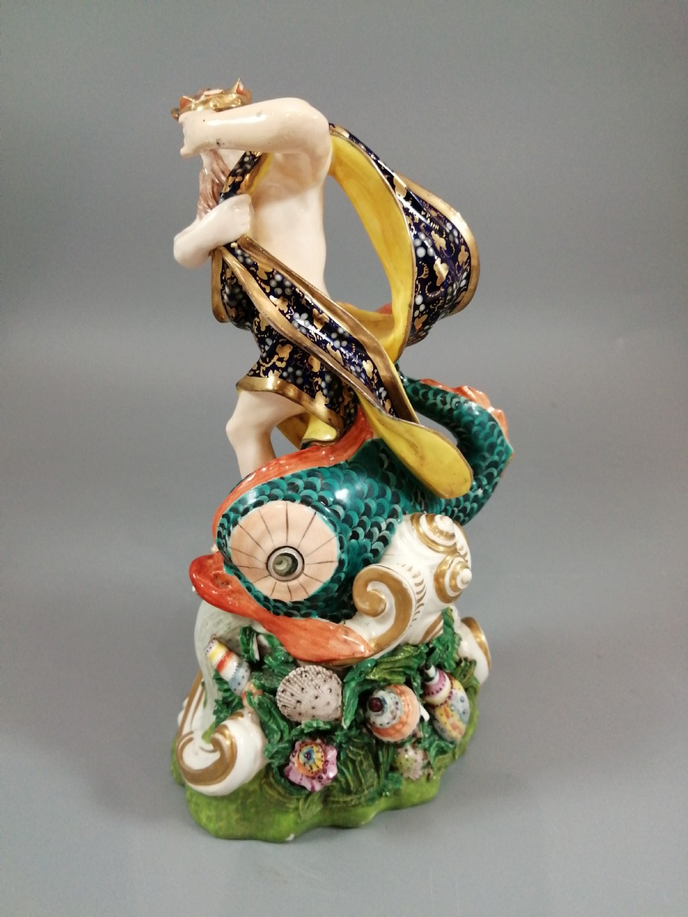 A Bloor Derby porcelain figure of Neptune standing atop a shell and rockwork base with sea creatures, wearing a crown and drapery decorated in gold leaf and blue enamel. View IV