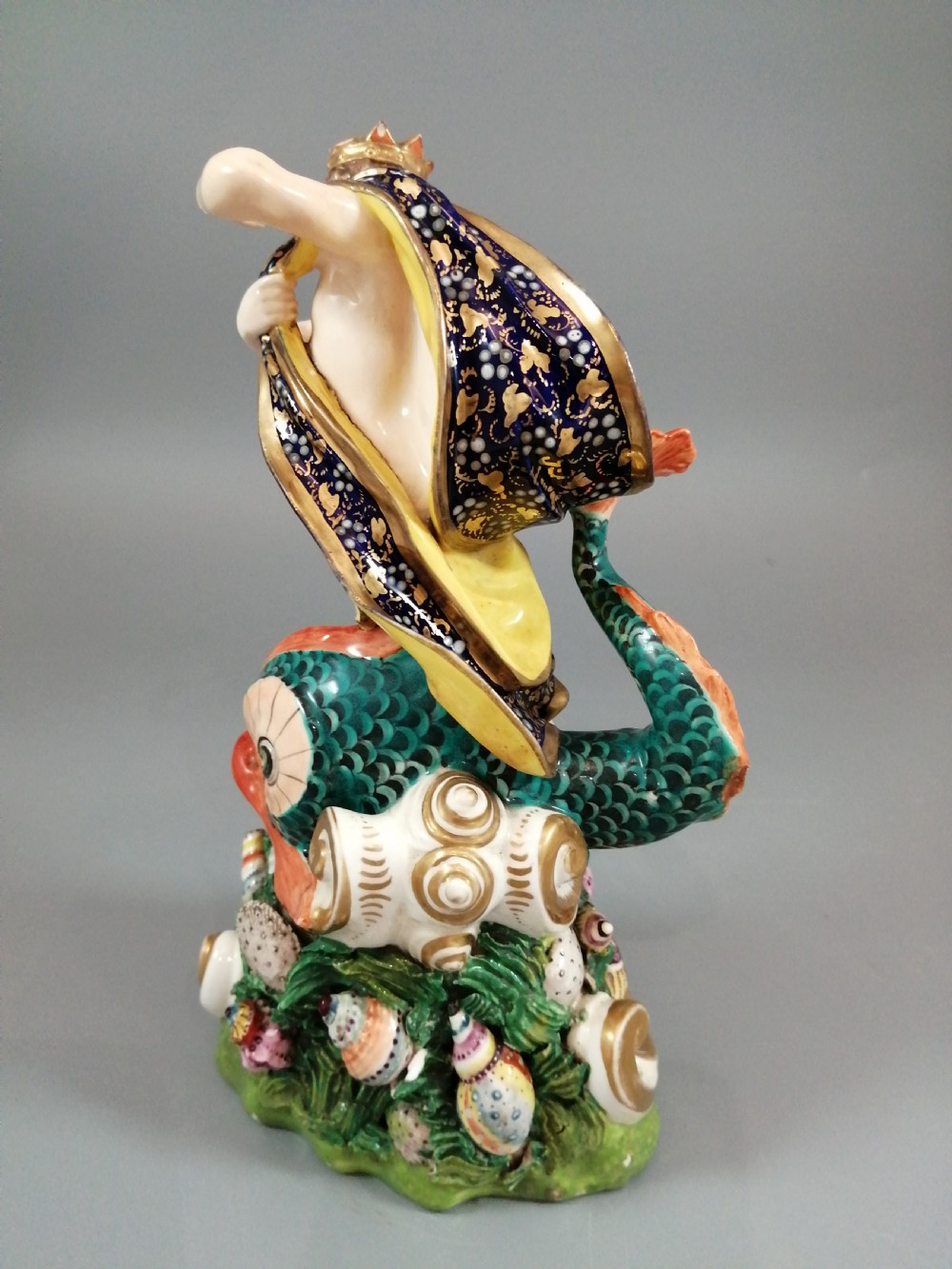 A Bloor Derby porcelain figure of Neptune standing atop a shell and rockwork base with sea creatures, wearing a crown and drapery decorated in gold leaf and blue enamel. View V