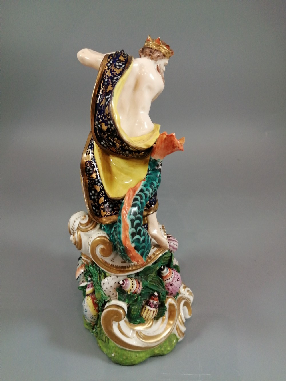 A Bloor Derby porcelain figure of Neptune standing atop a shell and rockwork base with sea creatures, wearing a crown and drapery decorated in gold leaf and blue enamel. View VI