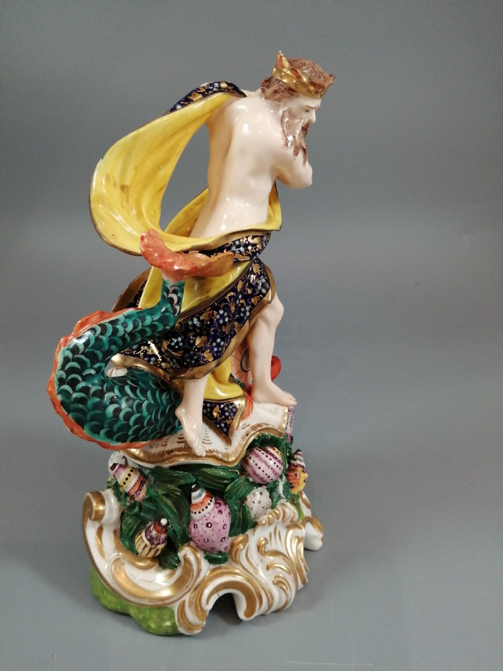 A Bloor Derby porcelain figure of Neptune standing atop a shell and rockwork base with sea creatures, wearing a crown and drapery decorated in gold leaf and blue enamel. View VII