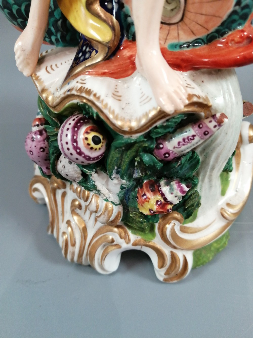 A Bloor Derby porcelain figure of Neptune standing atop a shell and rockwork base with sea creatures, wearing a crown and drapery decorated in gold leaf and blue enamel. View X