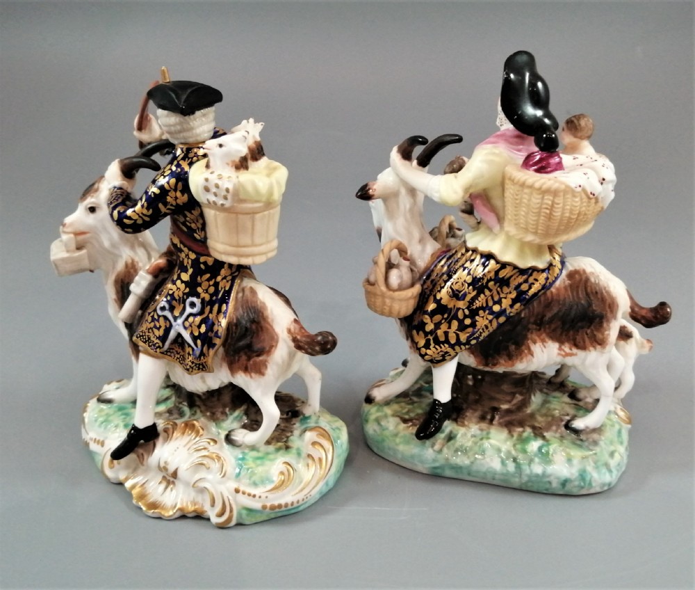 A pair of painted porcelain figurines depicting a man and woman in 18th-century attire riding goats with cobalt blue gilded jackets on rococo scroll bases. View III