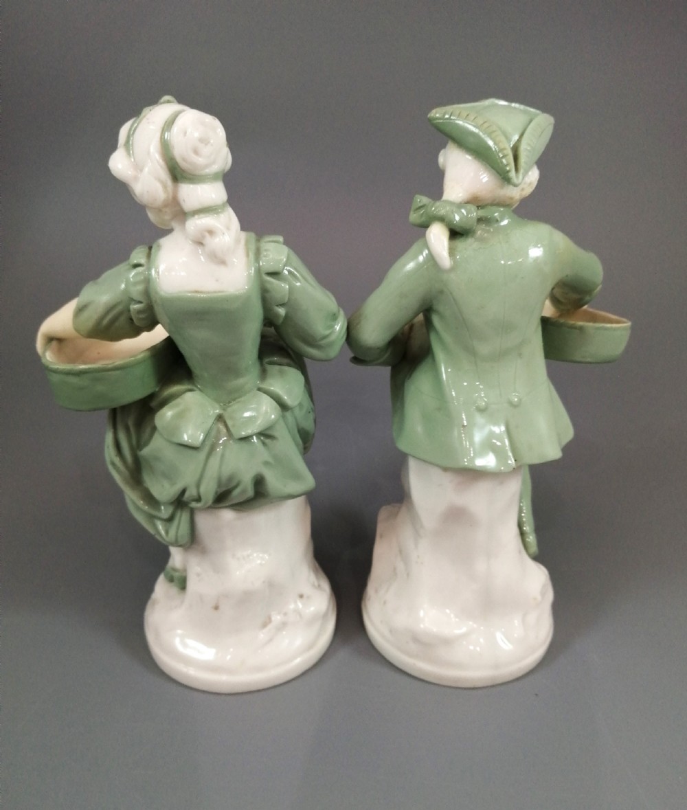 A pair of Victorian Minton celadon green and white porcelain figurines depicting a seated man and woman holding oval dishes on circular bases. View V
