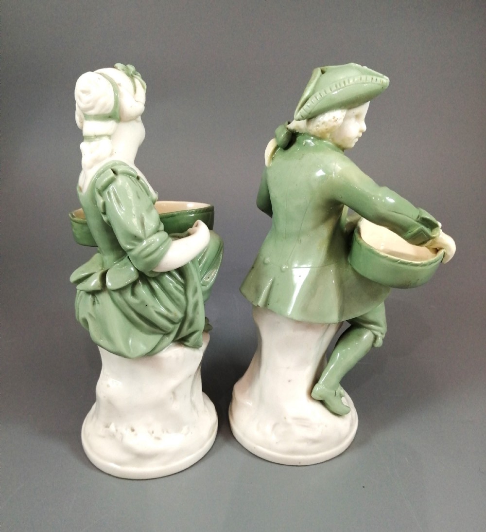 A pair of Victorian Minton celadon green and white porcelain figurines depicting a seated man and woman holding oval dishes on circular bases. View VI