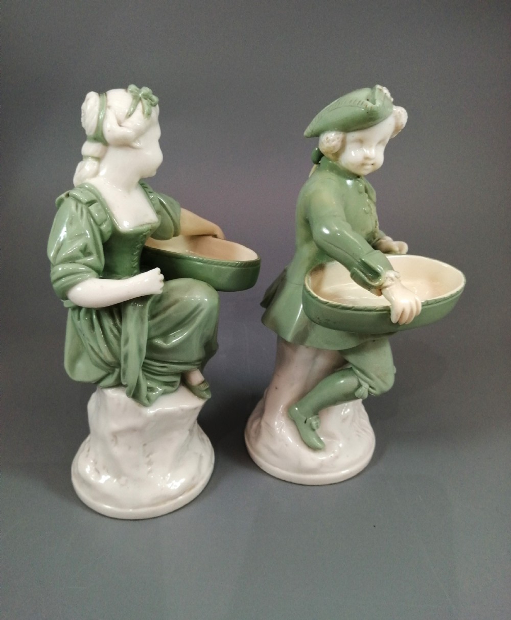 A pair of Victorian Minton celadon green and white porcelain figurines depicting a seated man and woman holding oval dishes on circular bases. View VII