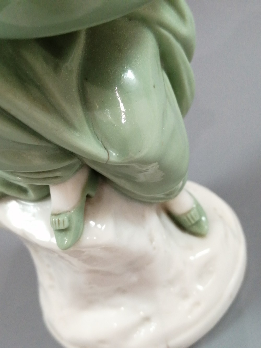 A pair of Victorian Minton celadon green and white porcelain figurines depicting a seated man and woman holding oval dishes on circular bases. View XIII