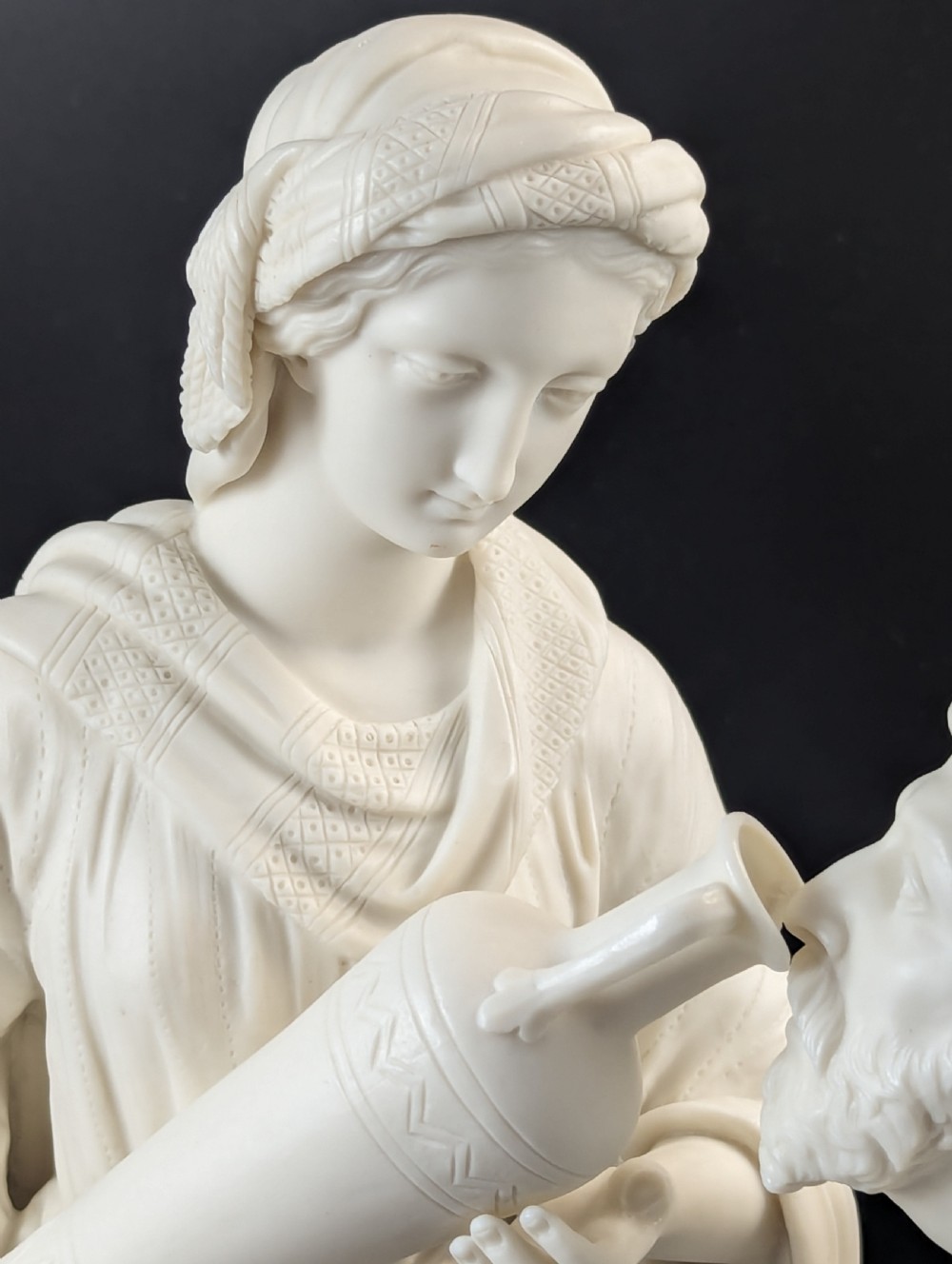 An off-white Parian porcelain sculpture depicting Rebekah offering water from an amphora to a kneeling man beside a textured stone well. View XI
