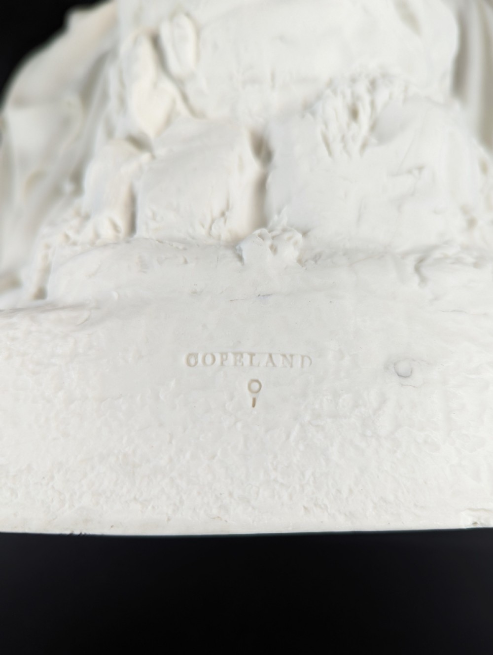An off-white Parian porcelain sculpture depicting Rebekah offering water from an amphora to a kneeling man beside a textured stone well. View XV