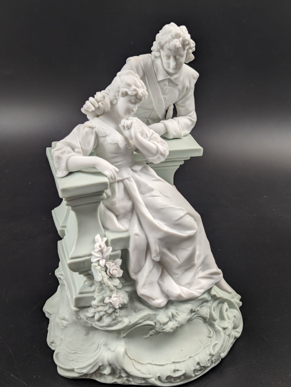 A white and pale green parian porcelain figurine depicting a courtly man and woman interacting beside a balustrade. View VII