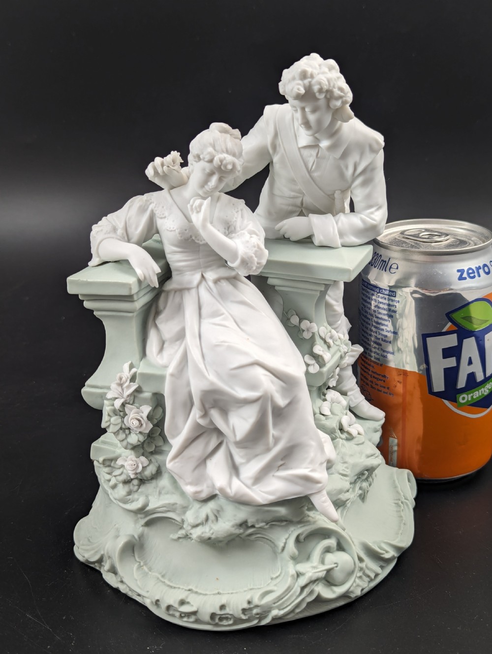 A white and pale green parian porcelain figurine depicting a courtly man and woman interacting beside a balustrade. View IX