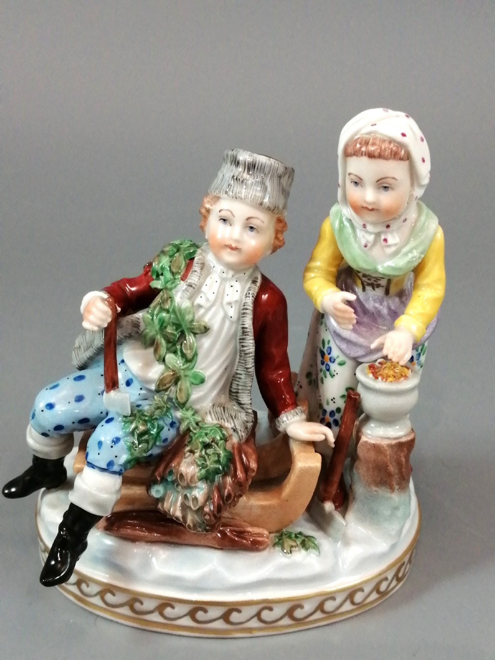 A Carl Thieme Potschappel hand-painted porcelain figurine depicting a young couple in eighteenth-century winter costume beside a sledge and brazier.