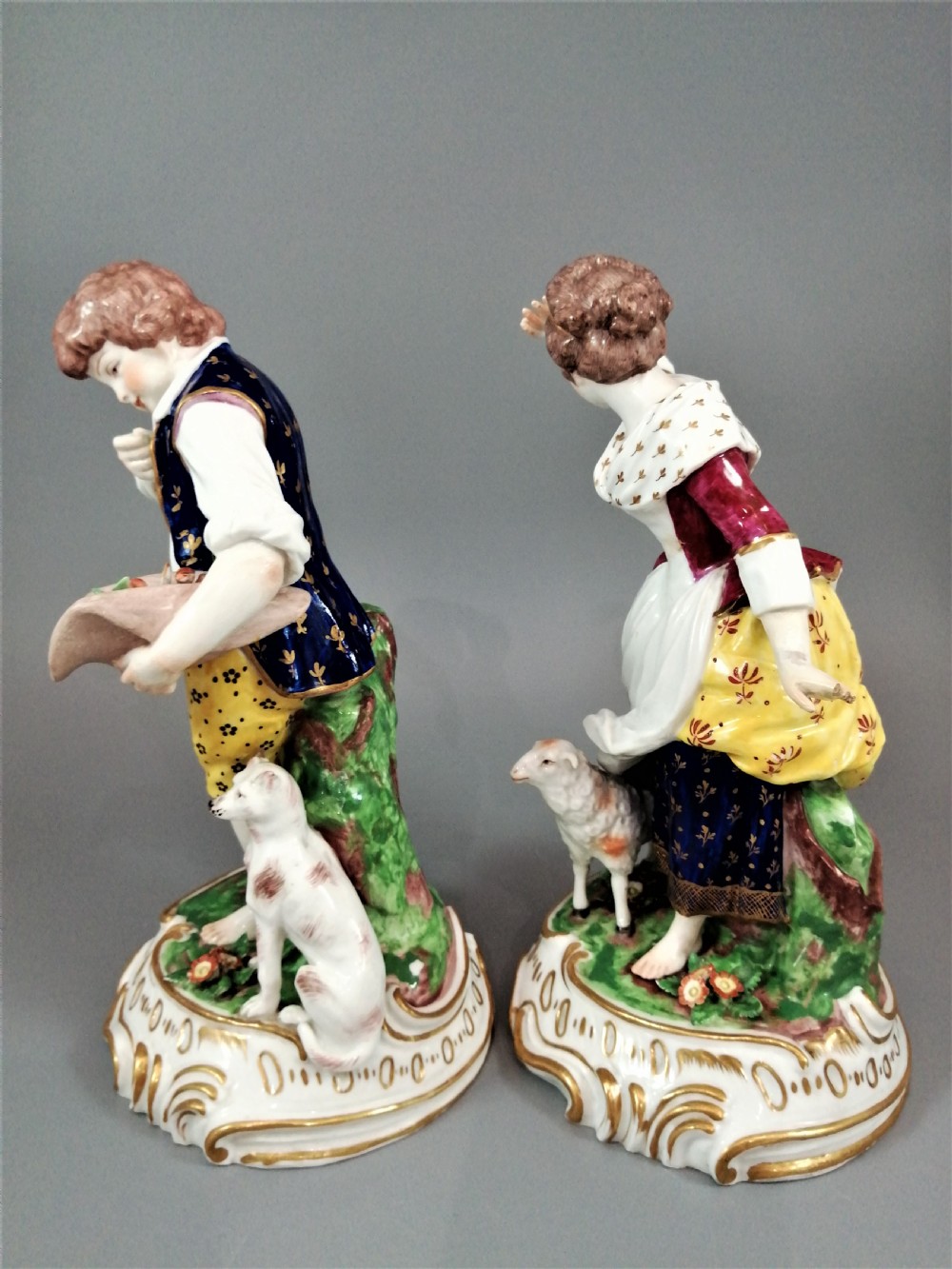 A pair of 19th-century French Samson porcelain figurines depicting a young boy with a basket of fruit and a dog alongside a shepherdess with a lamb, decorated with polychrome enamels and gilded scroll bases. View II