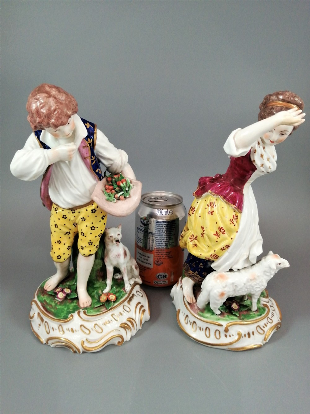 A pair of 19th-century French Samson porcelain figurines depicting a young boy with a basket of fruit and a dog alongside a shepherdess with a lamb, decorated with polychrome enamels and gilded scroll bases. View VI