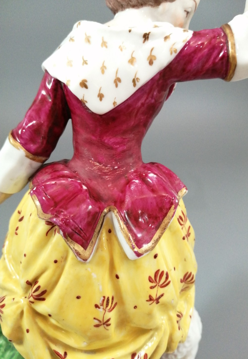 A pair of 19th-century French Samson porcelain figurines depicting a young boy with a basket of fruit and a dog alongside a shepherdess with a lamb, decorated with polychrome enamels and gilded scroll bases. View X
