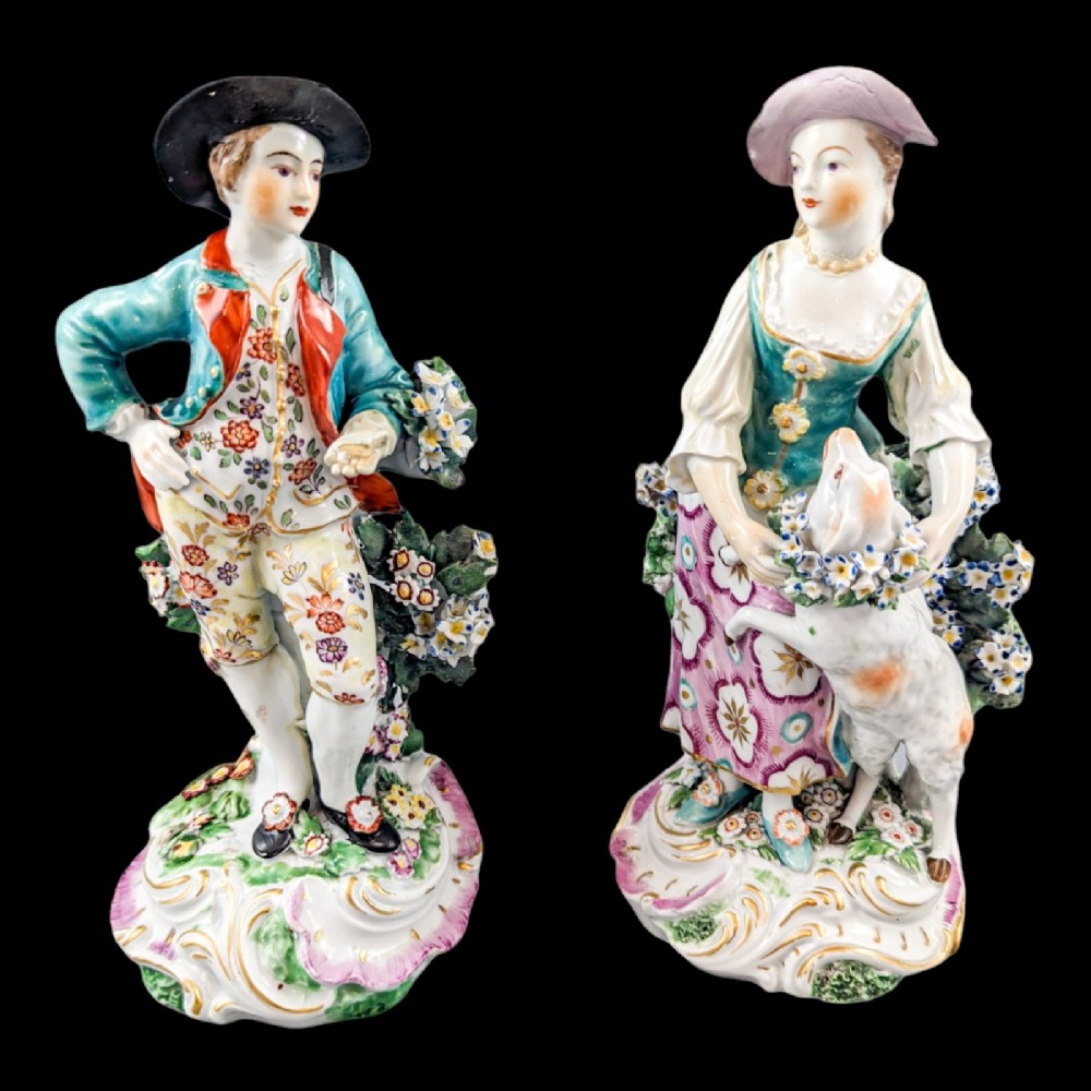 A pair of eighteenth-century Derby soft-paste porcelain figurines depicting a shepherd and shepherdess adorned in floral-patterned garments with garlands on scroll bases.