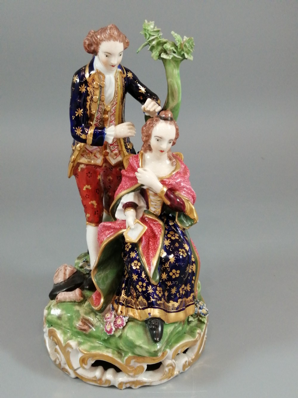 An early nineteenth-century painted porcelain figurine depicting a male court hairdresser styling a seated ladys hair on a rococo scroll base.
